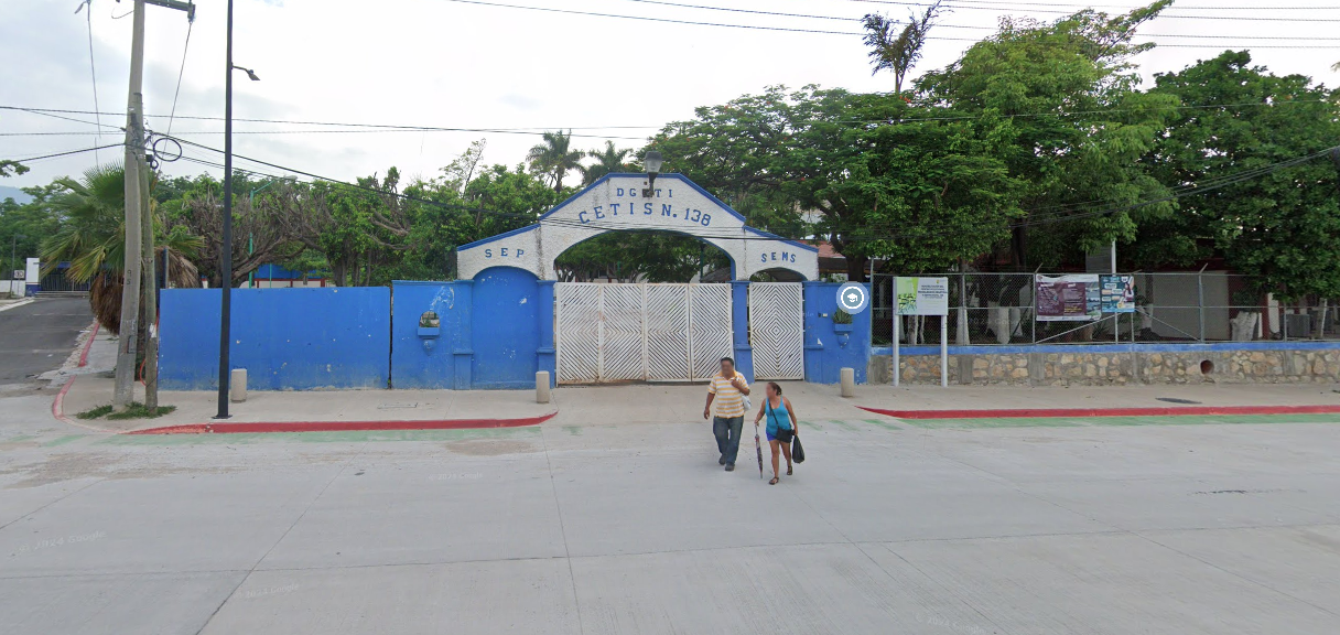 Fotografía en la que se muestra la entrada del plantel conformada por muros de color azul. En medio de los muros hay un portón de color blanco. En la parte superior del portón hay un arco de color blanco en el que en letras grandes azules dice CETIS NÚMERO 138. 
